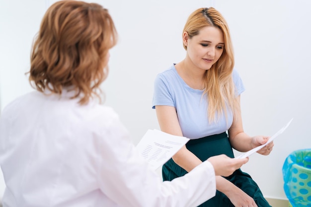 Una doctora profesional transmite a una joven embarazada con cabello rubio los resultados e informes de las pruebas realizadas. Concepto de maternidad feliz y saludable.