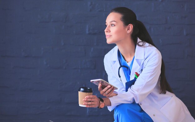 Doctora sentada con teléfono móvil y tomando café