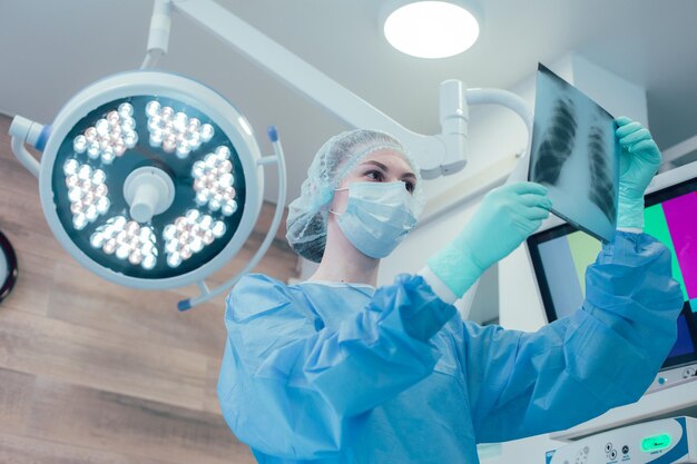 Doctora seria en la sala de operaciones haciendo un diagnóstico mientras mira la imagen de la radiografía de tórax