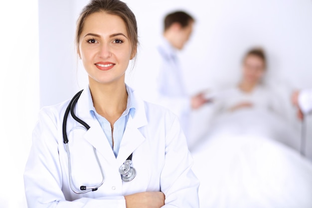 Doctora sonriendo en el fondo con un paciente en la cama y dos médicos.