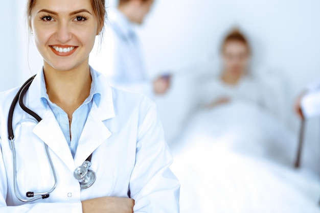 Doctora sonriendo en el fondo con un paciente en la cama y dos médicos.