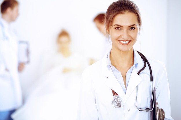 Doctora sonriendo en el fondo con un paciente en la cama y dos médicos.