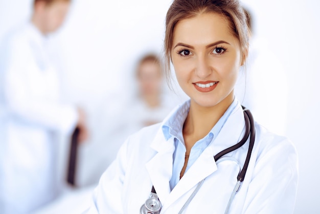 Doctora sonriendo en el fondo con un paciente en la cama y dos médicos.