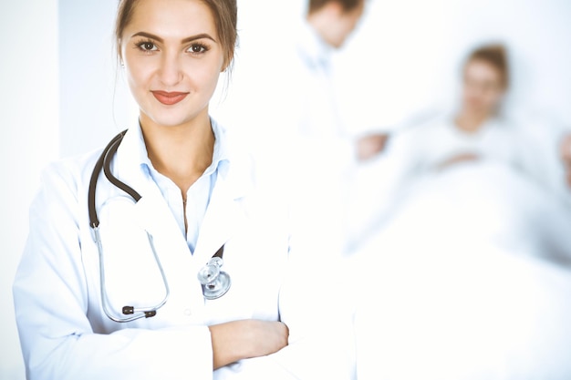 Doctora sonriendo en el fondo con un paciente en la cama y dos médicos.