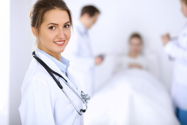 Doctora sonriendo en el fondo con un paciente en la cama y dos médicos.