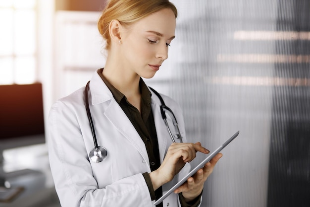 Una doctora sonriente alegre que usa una tableta en una clínica soleada. Retrato de una mujer médica amigable en el trabajo. Perfecto servicio médico en el hospital. concepto de medicina.