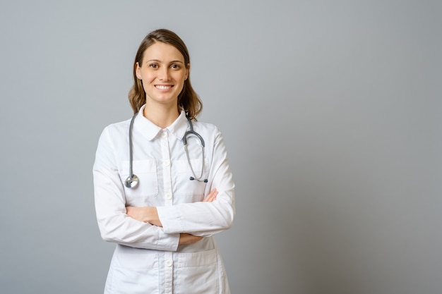 Doctora sonriente en bata de laboratorio con los brazos cruzados sobre la pared gris