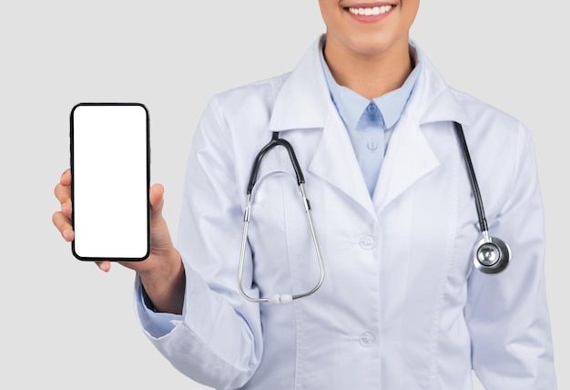 Una doctora sonriente con bata de laboratorio presenta un teléfono inteligente con una pantalla en blanco