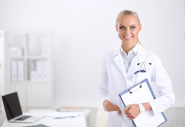 Doctora sonriente con una carpeta en uniforme de pie en el hospital