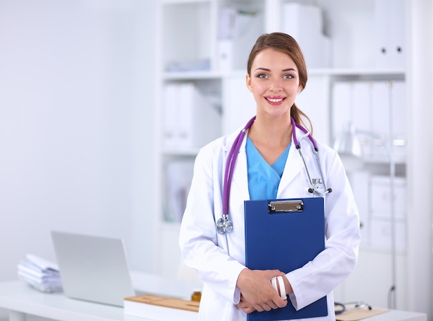 Doctora sonriente con una carpeta en uniforme de pie en el hospital