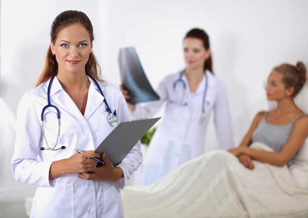 Foto doctora sonriente con una carpeta en uniforme de pie en el hospital