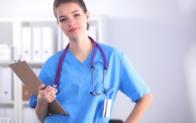 Doctora sonriente con una carpeta en uniforme de pie en el hospital