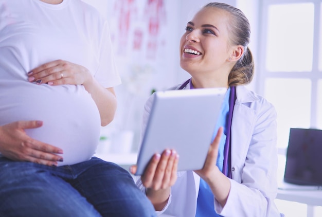 Foto una doctora sonriente muestra imágenes en la tableta a una joven embarazada en el hospital