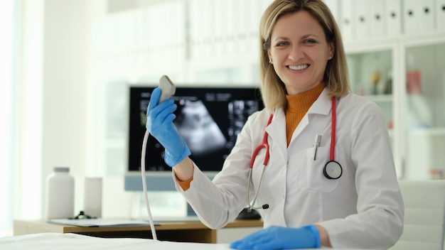 Una doctora sonriente sosteniendo una sonda de ultrasonido en sus manos en la clínica