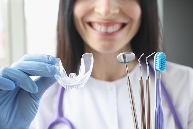 Doctora sonriente sostiene protector bucal de plástico transparente e instrumentos estomatológicos en su mano