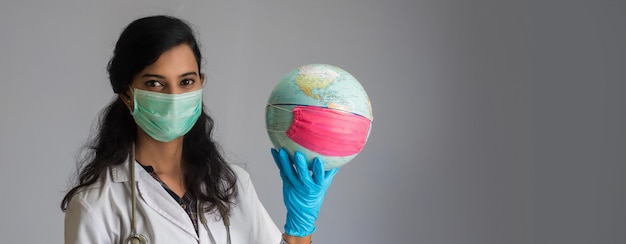 Doctora sosteniendo el globo del mundo con una mascarilla de medicina. Epidemia mundial del concepto de coronavirus.