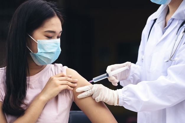 Doctora sosteniendo una jeringa haciendo dosis de inyección de vacunación covid 19 en el hombro de la paciente con máscara. F