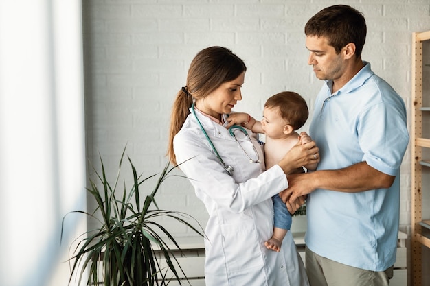 Doctora sosteniendo a un niño pequeño que vino a una cita médica con su padre