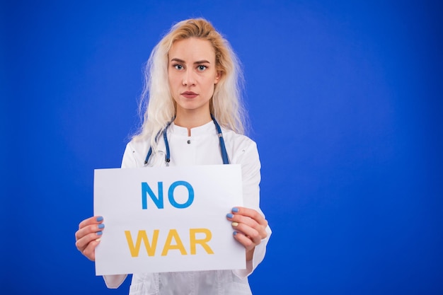 Una doctora sostiene un cartel de no guerra en un fondo azul.