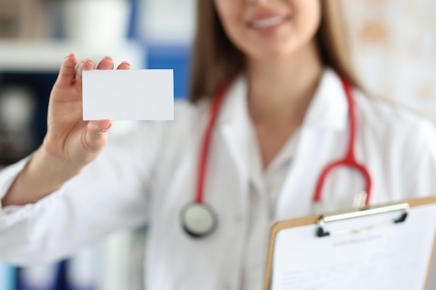 Foto doctora sostiene una tarjeta de presentación blanca frente a su consultorio médico