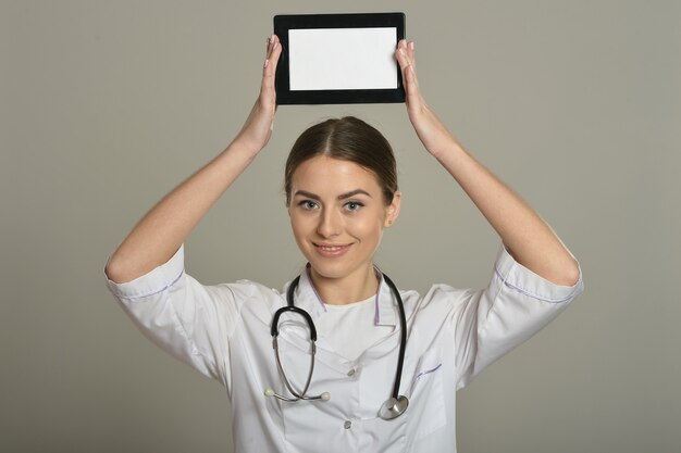 Doctora con tablet pc, de pie sobre fondo gris