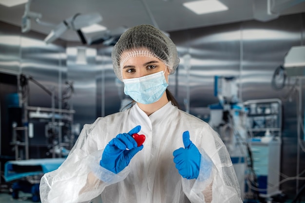 Una doctora con uniforme azul y una máscara sostiene un pequeño corazón rojo con las manos como símbolo en el quirófano Concepto de medicina una enfermera con un amor de corazón por los pacientes