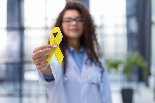 Foto la doctora con uniforme blanco sostiene una cinta amarilla en la mano, símbolo de la lucha contra el problema del tumor del gato de los suicidios y su prevención.