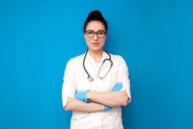 Doctora en uniforme se encuentra con los brazos cruzados sobre fondo azul.