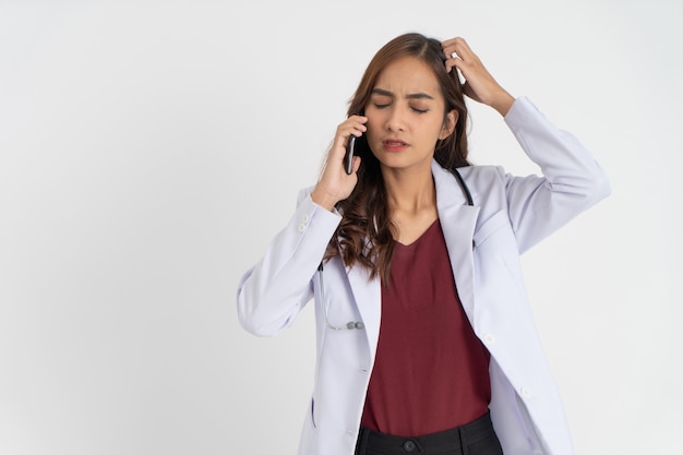 Una doctora vestida con un uniforme blanco confundida con un gesto de angustia mientras realiza una llamada telefónica