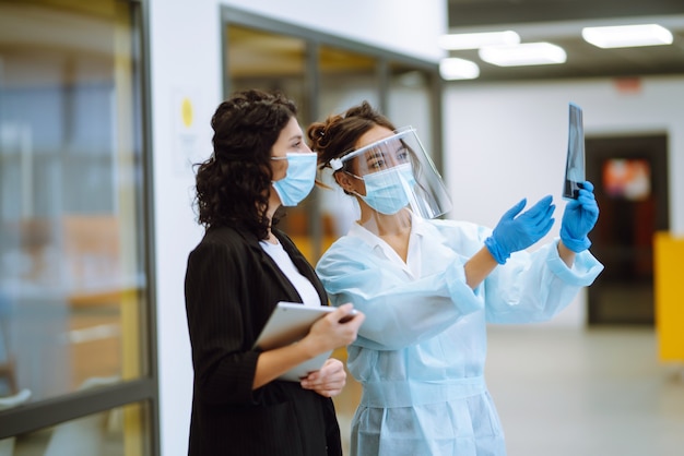 Una doctora con visera y guantes protectores examina una radiografía de un paciente