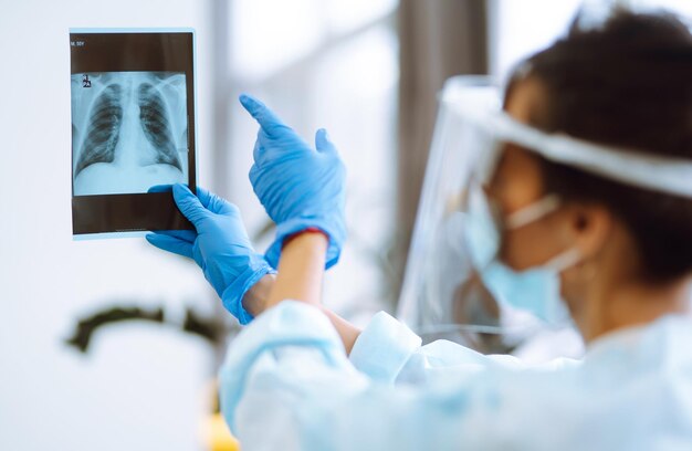 Una doctora con visera y guantes protectores examina una radiografía de un paciente