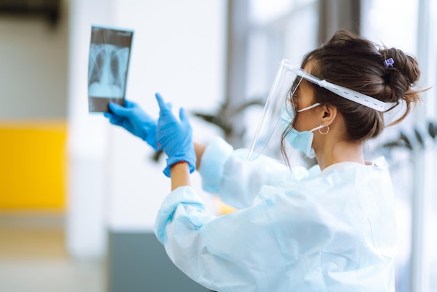 Una doctora con visera y guantes protectores examina una radiografía de un paciente