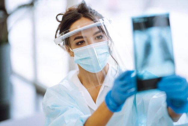 Una doctora con visera y guantes protectores examina una radiografía de un paciente