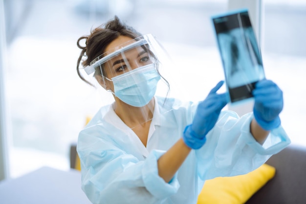 Una doctora con visera y guantes protectores examina una radiografía de un paciente