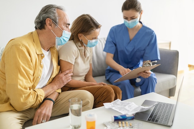 Foto doctora visitando a una pareja mayor en casa usando máscaras faciales durante el brote de gripe hablando de