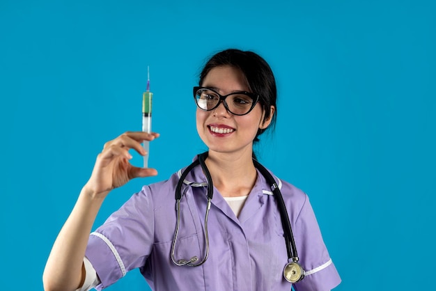 Doctora vistiendo bata blanca con jeringa sonriendo fondo de color sólido aislado