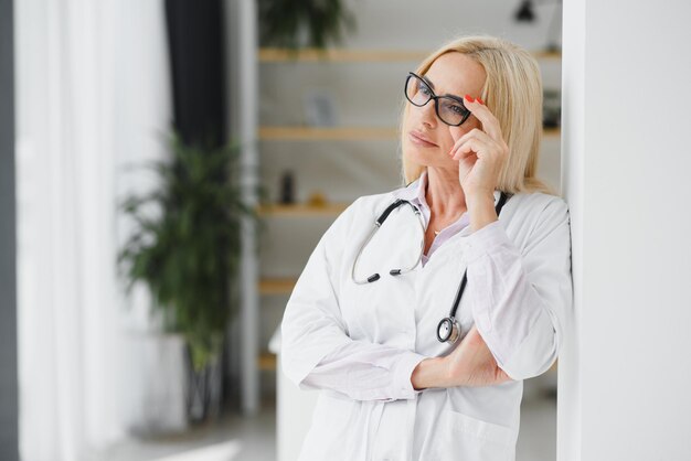 Doctora vistiendo bata de laboratorio y estetoscopio y sosteniendo portapapeles en sus manos mientras está de pie en el hospital