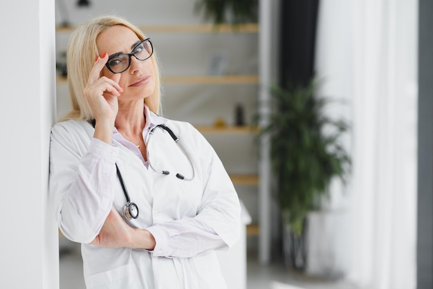 Doctora vistiendo bata de laboratorio y estetoscopio y sosteniendo portapapeles en sus manos mientras está de pie en el hospital