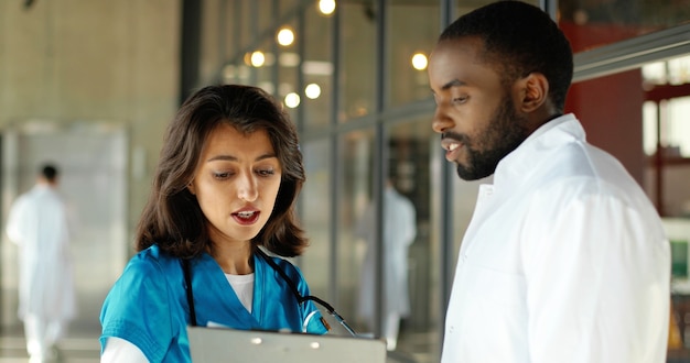 Doctores y doctores de razas mixtas hablando alegremente en la clínica. Hombre y mujer multiétnicos, médicos que tienen discusión en el hospital. Médico con enfermera. Doc y asistente. Conversacion.