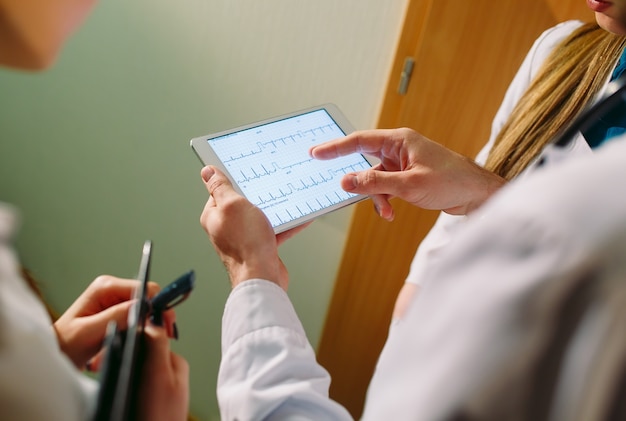 Doctores que discuten el cardiograma del paciente en la tableta.