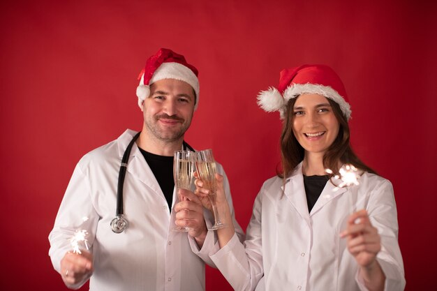 Doctores con sombreros de Santa Claus animando con copas de champán y sosteniendo bengalas