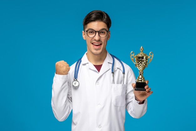 Doctors Day süßer junger gutaussehender Mann in Laborkittel und Brille, der aufregend eine goldene Trophäe hält