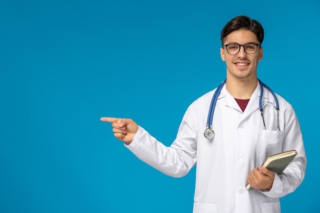 Doctors Day süßer junger gutaussehender Mann in Laborkittel und Brille, der lächelt und Notizbuch hält