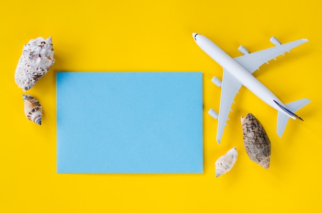 Documento azul vacío sobre fondo amarillo con conchas marinas y avión decorativo. Concepto de viaje de verano.