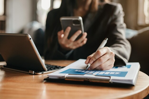 Documentos comerciales en el escritorio de la oficina con computadora portátil y teléfono inteligente y diagrama comercial gráfico y mujeres que trabajan en la oficina por la mañana.