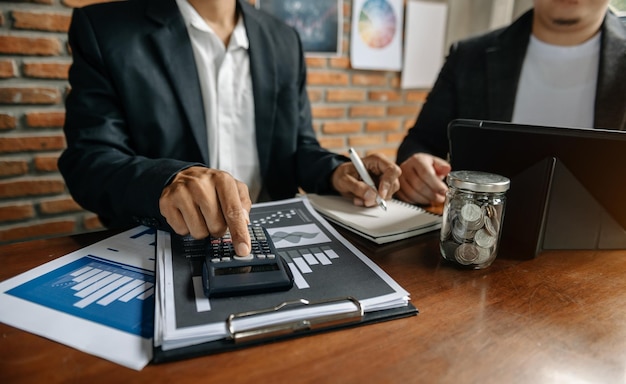 Documentos comerciales en la mesa de la oficina con teléfono inteligente y calculadora, tableta digital y negocio gráfico con diagrama de red social y dos colegas discutiendo datos que trabajan en officexA