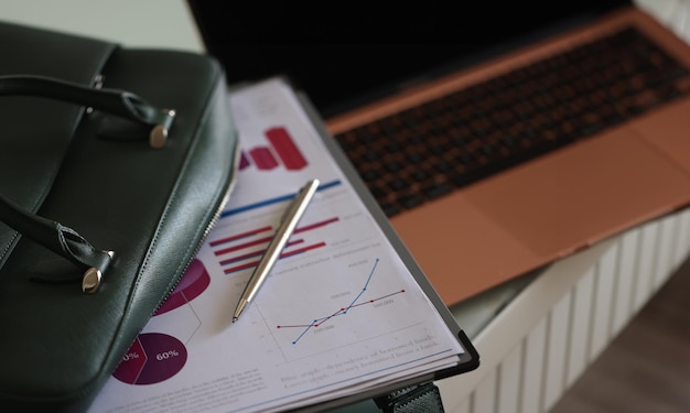 Documentos de clipboard e caneta de bolas deitados em uma bolsa de laptop verde aberta em close-up