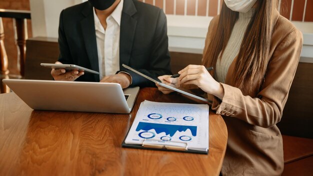 Documentos de negócios na mesa de escritório com smartphone tablet e laptop e dois colegas discutindo dados na luz da manhãxA