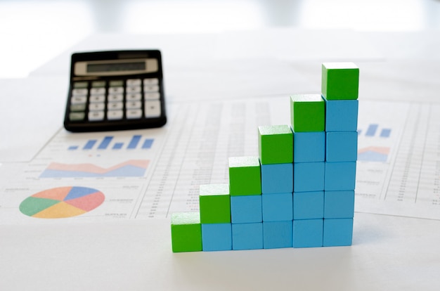 Documentos financieros, con cubos azules y verdes dispuestos en un gráfico de columnas como concepto de crecimiento, ingresos o ingresos.