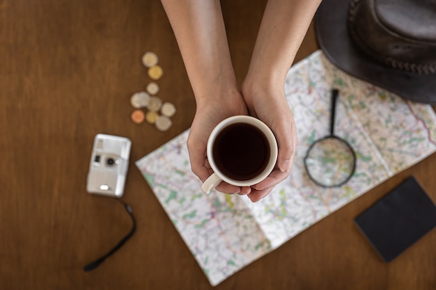 Documentos de lupa de mapa plano laico y una taza de café en manos de una mujer